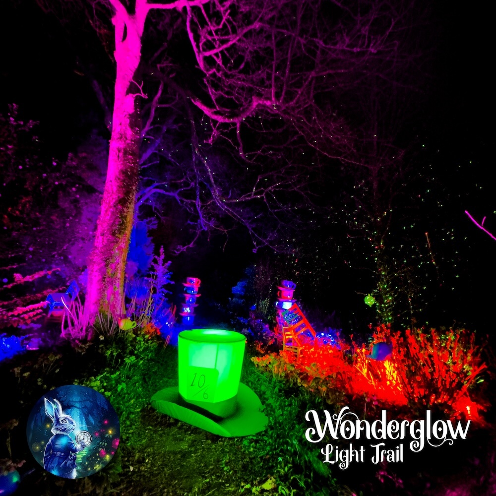 Glowing lights in different colours illuminating the mas hatter's glowing green hat and the trees behind it